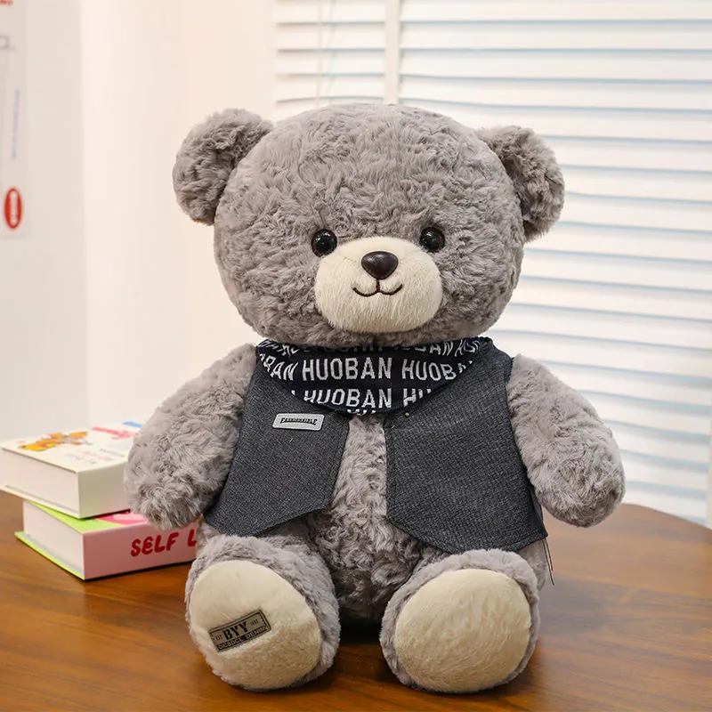 Grey teddy bear plush doll seated front-facing with curly fur, cream paw pads, and dark vest